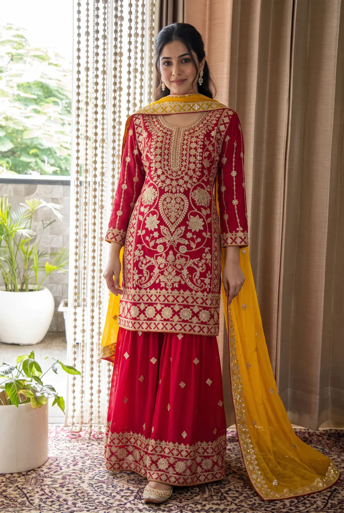A woman wearing a red embroidered kurti, sharara and yellow dupatta